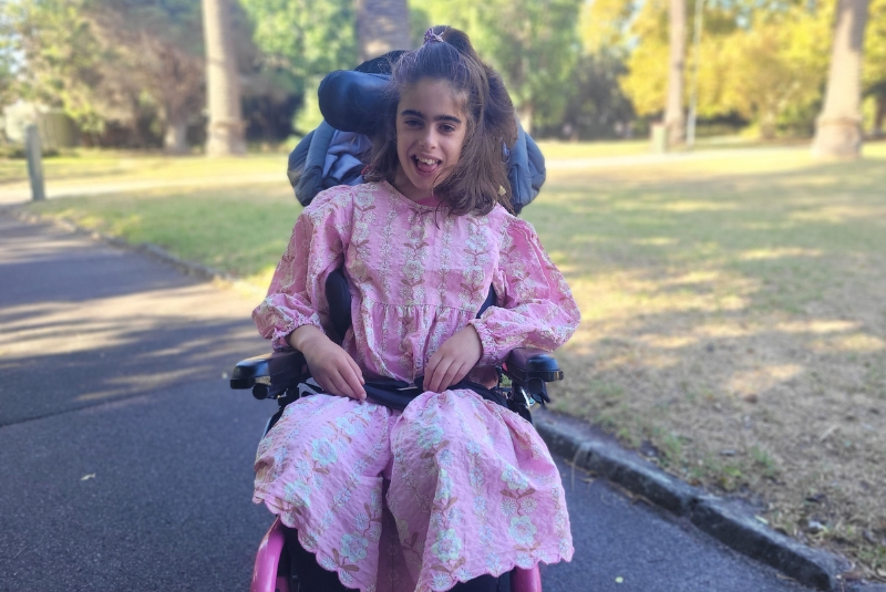Gitty smiling whilst sitting in her wheelchair in the park